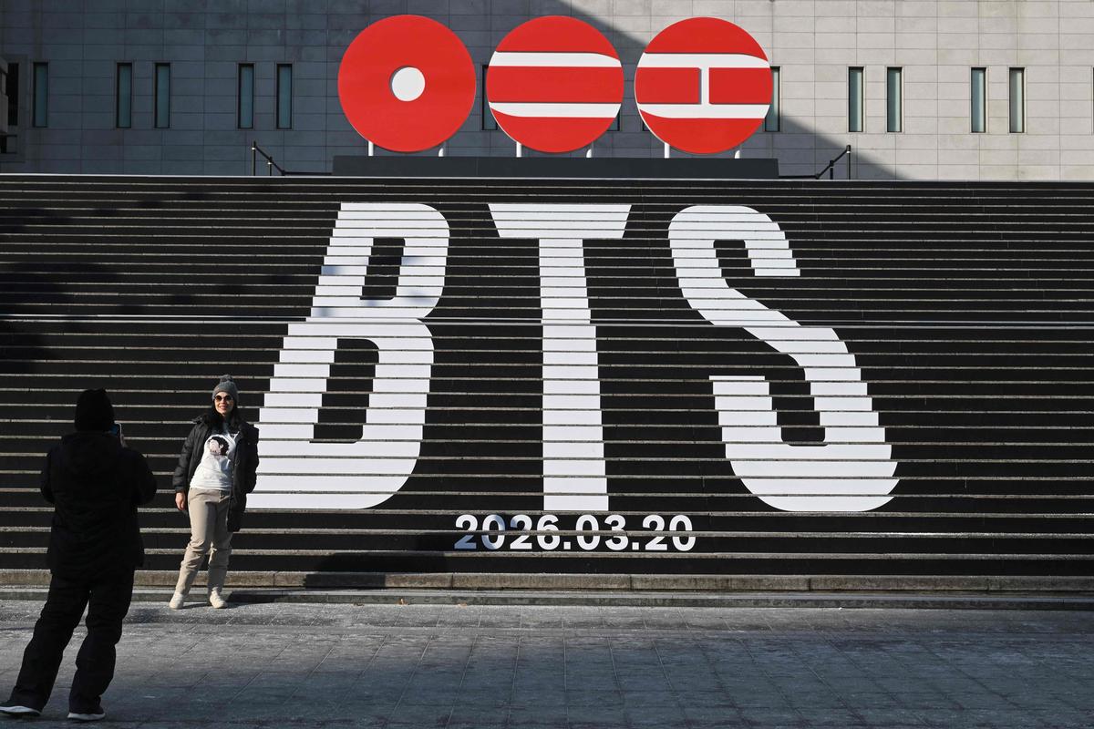 Uma mulher posa para uma foto em frente às escadas exibidas com o logotipo do álbum 2026 do BTS e a data de lançamento na Praça Gwanghwamun em Seul em 14 de janeiro de 2026. As megaestrelas do K-pop BTS lançarão uma turnê mundial de retorno a partir de abril, disse a gravadora da banda em 14 de janeiro. 