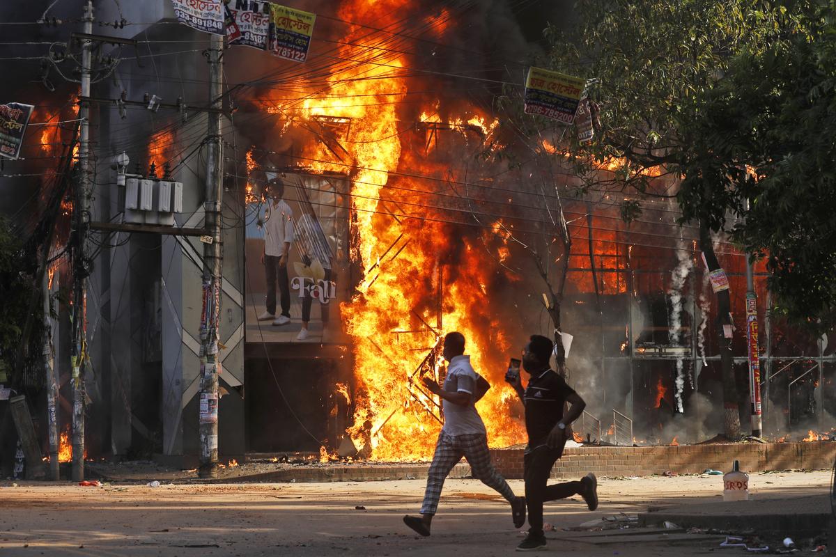 Men run past a shopping mall that was set on fire by protesters during a demonstration against Prime Minister Sheikh Hasina and her government to demand justice for victims killed in recent deadly clashes across the country, in Dhaka, Bangladesh, August 4, 2024. 