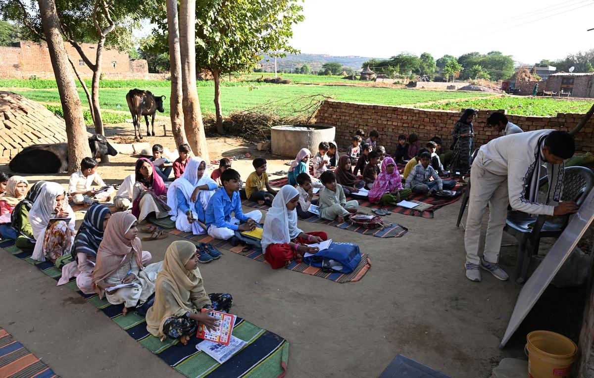 A teacher of a primary school in Padodiyabass teaching students beside an open field, with no arrangement for toilets, drinking water or electricity. 