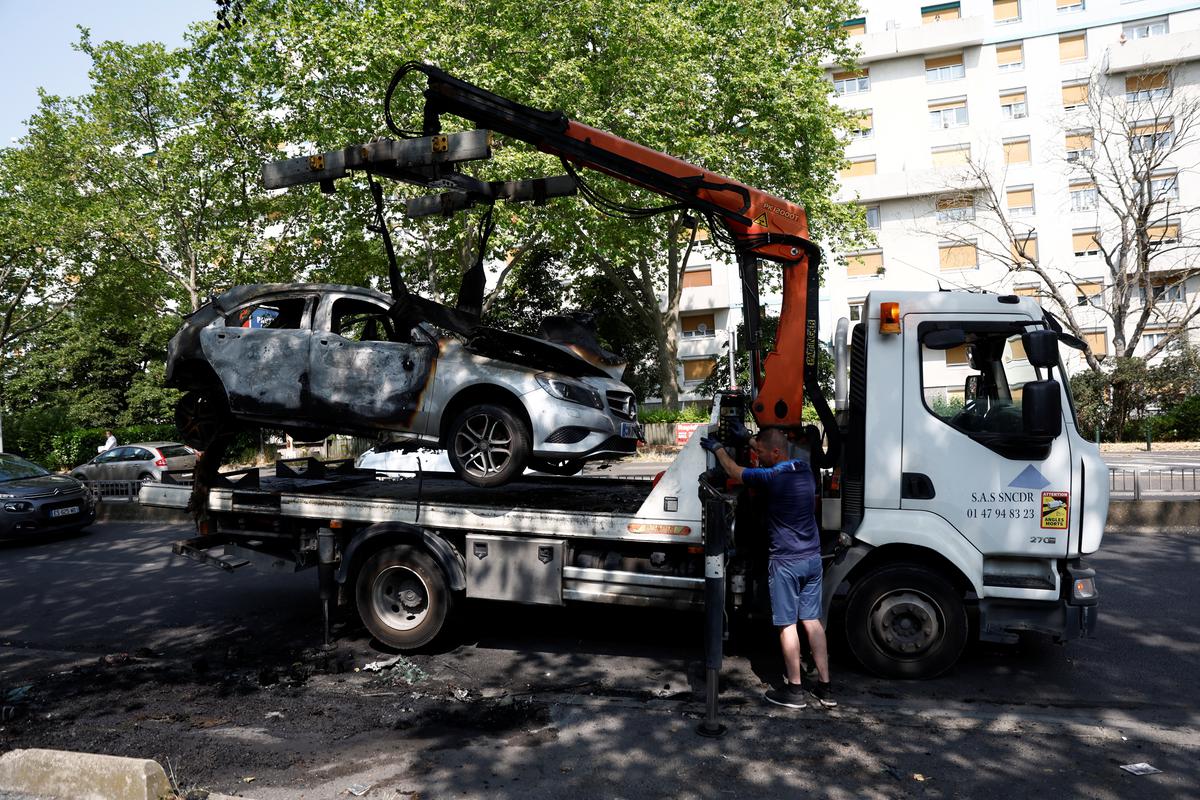 जून में फ्रांस के पेरिस उपनगर नैनटेरे में यातायात रोकने के दौरान एक फ्रांसीसी पुलिस अधिकारी द्वारा मारे गए 17 वर्षीय किशोर की मौत के अगले दिन युवाओं और पुलिस के बीच झड़प के दौरान जलाई गई एक कार को सड़क से हटा दिया गया है। 28, 2023. 