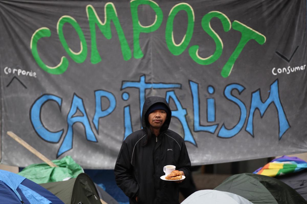 A man stands in front of an anti-capitalism poster in London.