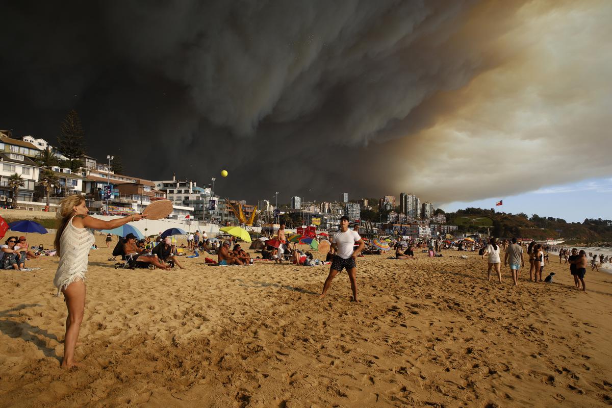 Vacationers play paddle ball on a beach backdropped by a darkening sky caused by smoke from nearby forest fires, in Viña del Mar, Chile, Friday, February 2, 2024. 
