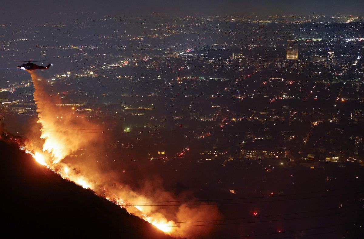 A firefighting helicopter drops water as the Sunset Fire burns in the Hollywood Hills with evacuations ordered in Los Angeles, California on January 8, 2025.