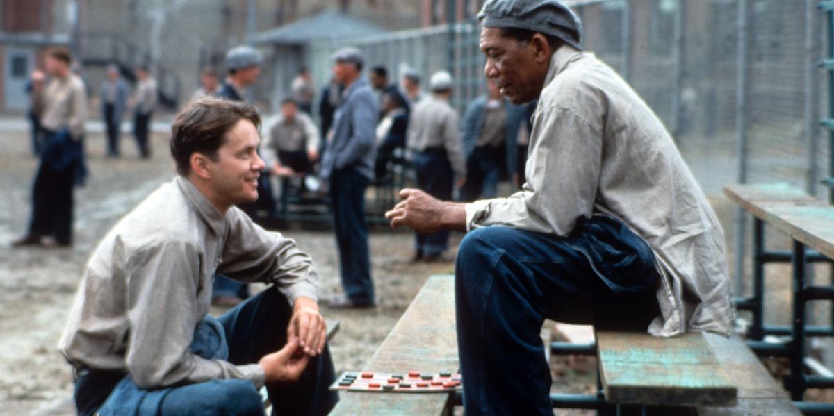 Tim Robbins and Morgan Freeman sit on the benches outside, playing checkers and talking in a scene from the film