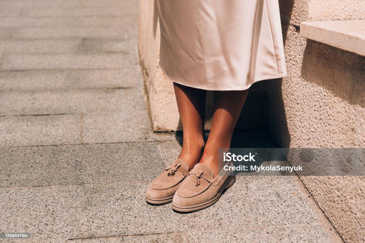 Portrait of fashionable women in beige dress and stylish suede loafer shoes posing in the street