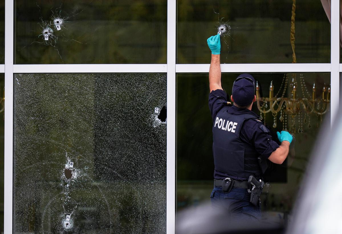 A Royal Canadian Mounted Police (RCMP) officer places evidence markers beside bullet holes in the windows of a cafe, in Surrey, British Columbia, Thursday, Aug. 7, 2025, as police investigate after shots were fired for the second time within a month at Kapil Sharma’s Kap’s Cafe.