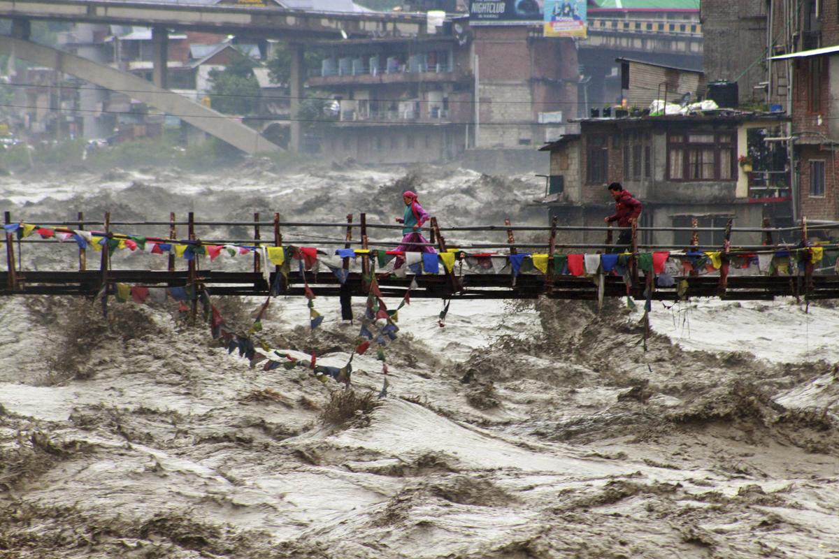 Residents run across a bridge over the flooding Beas River following incessant rains in Kullu Residents run across a bridge over the flooding Beas River following incessant rains in Kullu