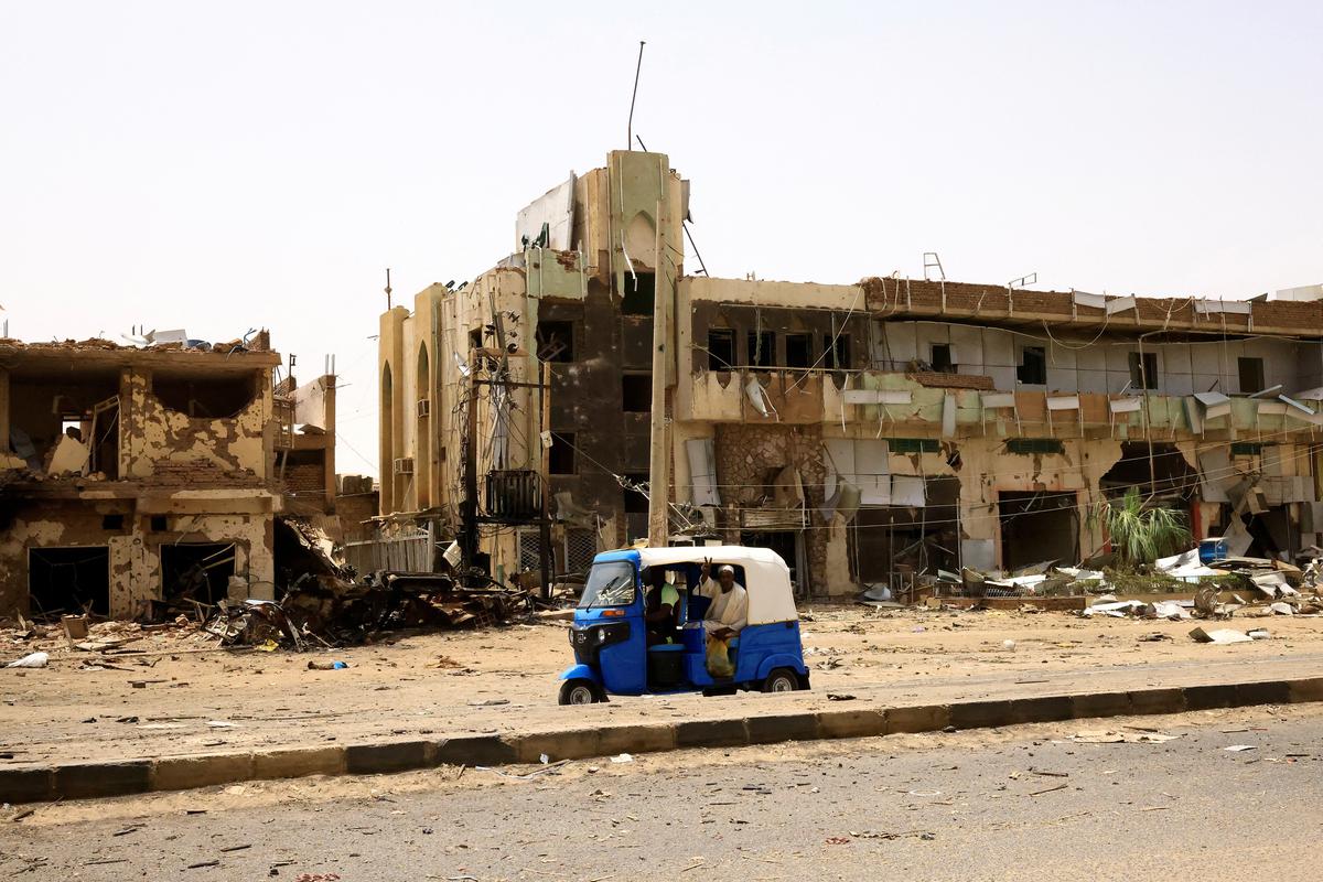 Orang-orang berjalan melewati kendaraan dan bangunan yang rusak di pasar pusat selama bentrokan antara Pasukan Dukungan Cepat paramiliter dan tentara di Khartoum Utara, Sudan.