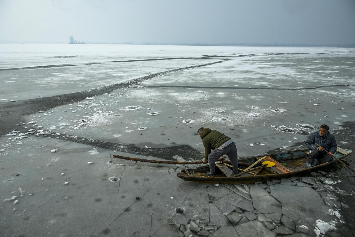 A boatman tries to break the ice with a wooden stick while making his way through a partially frozen surface of Dal Lake in Srinagar. File