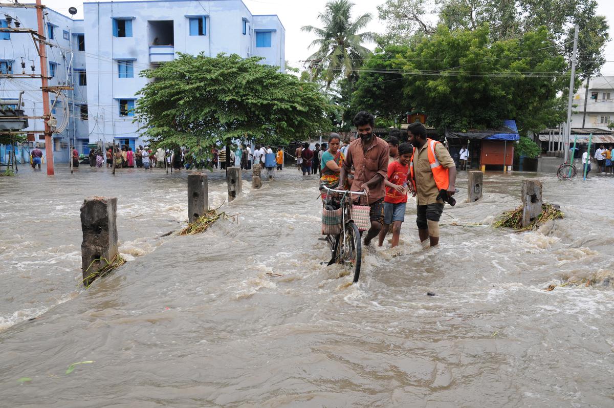People cross the submerged bridge across Pichaikaran Pallam Canal in Erode in Tamil Nadu on November 22, 2023
