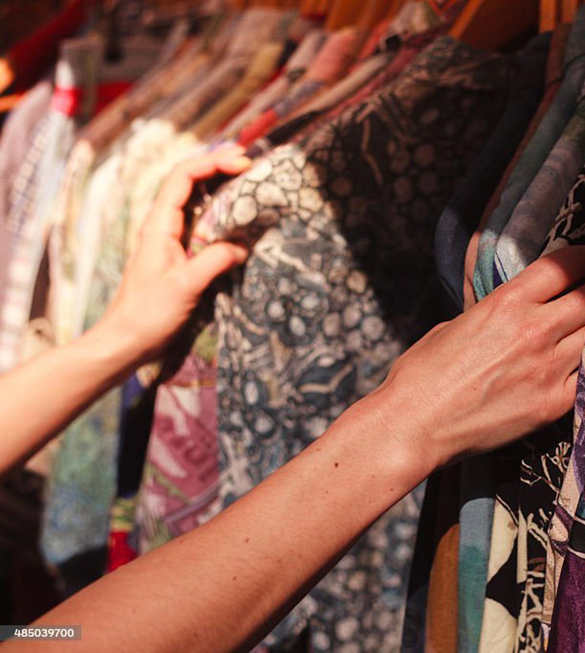 A young woman is browsing a rail of clothes at a street market