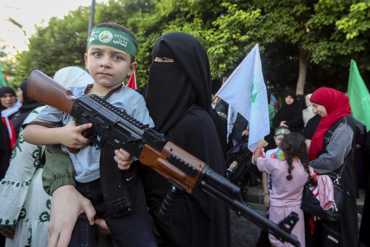 A supporter of the Islamist Hamas movement carries her son, who holds a machine gun toy during a protest in the southern port city of Sidon, Lebanon to condemn the killing of Hamas political chief Ismail Haniyeh.