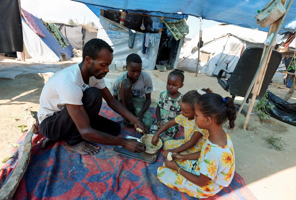 Displaced Palestinian man Tayseer Obaid, who lives in a tent with his wife and eight children and has documented his struggle to obtain food and aid amid a hunger crisis, eats with his children outside their tent, in Deir al-Balah in the central Gaza Strip, on August 7, 2025.