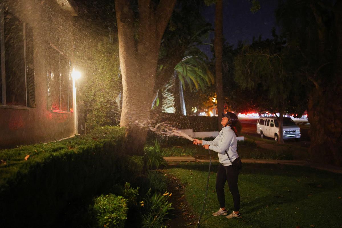 A woman waters the area in front of her house before leaving following an evacuation order, as a wildfire burns in the Pacific Palisades neighborhood of west Los Angeles, in Santa Monica, California, U.S. on January 7, 2025.