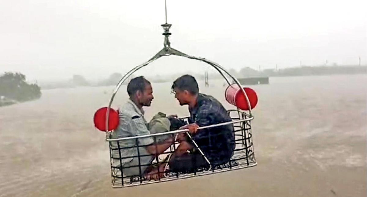 People sit in the Indian Coast Guard helicopter winch cradle during a rescue operation in the flood-affected Porbandar and Devbhoomi Dwarka districts where people were stranded over rooftops and other makeshift structures, on August 29, 2024.