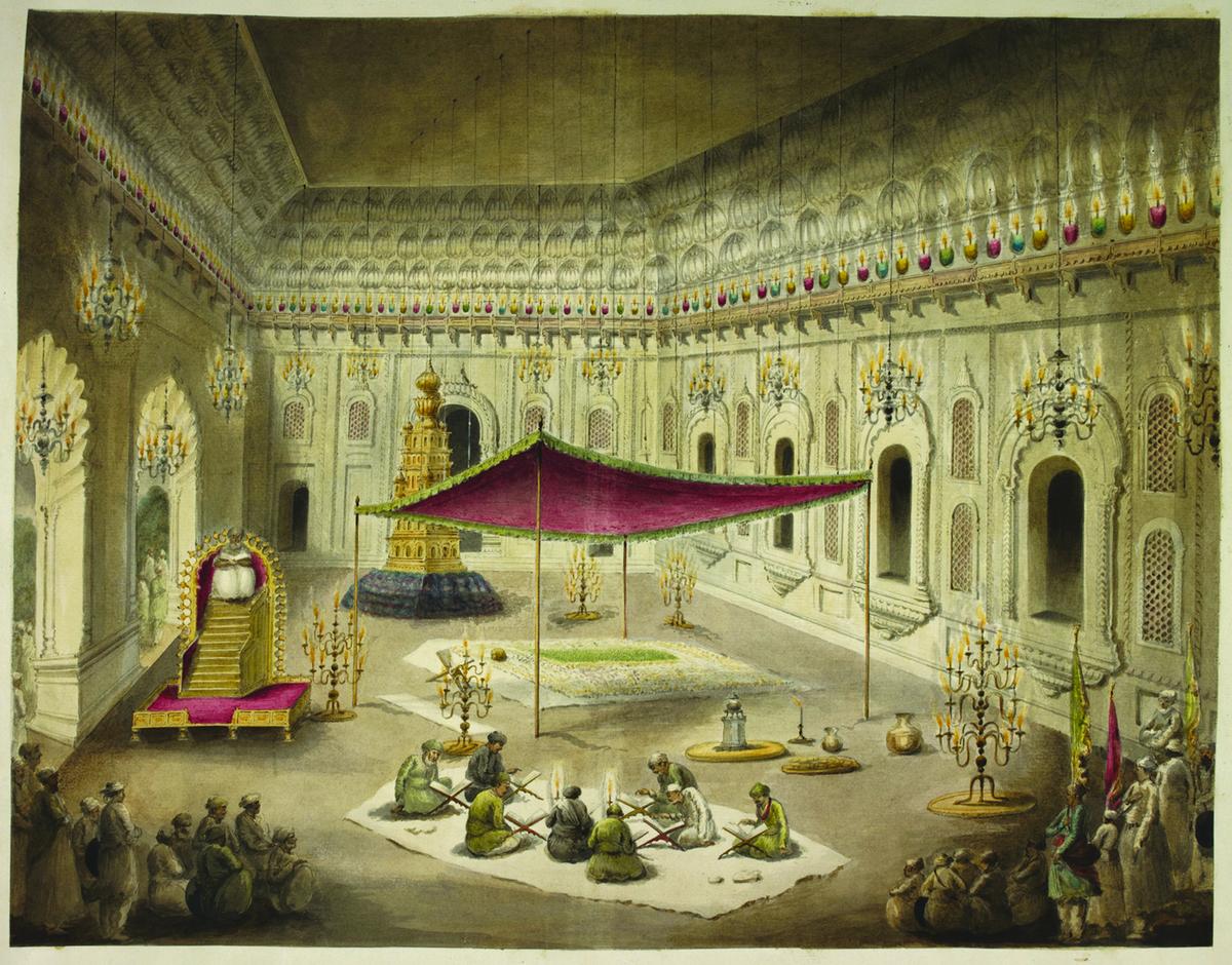 The simple grave of Asaf al-Daula under a canopy inside the Imambara, with imams reading the Koran. The hall is brilliantly lit with coloured girandoles attached to the parapet beneath the ceiling, and by three rows of chandeliers suspended from the latter. The simple grave of Asaf al-Daula under a canopy inside the Imambara, with imams reading the Koran. The hall is brilliantly lit with coloured girandoles attached to the parapet beneath the ceiling, and by three rows of chandeliers suspended from the latter.