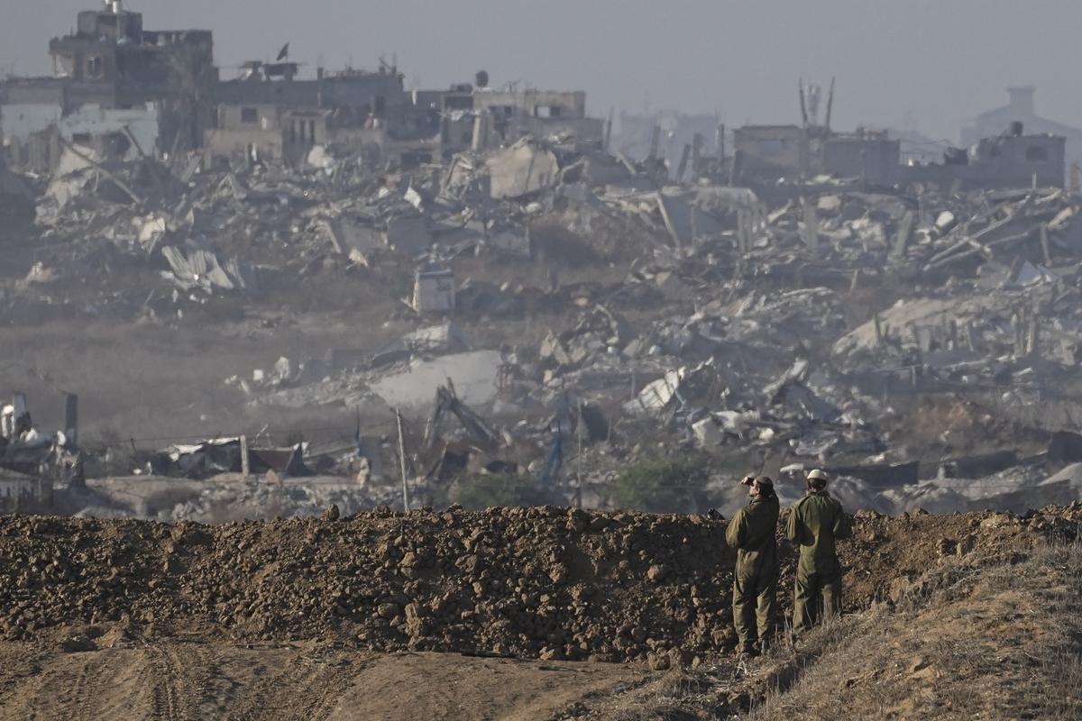 Israeli soldiers look at a destroyed part of Gaza City from their position on the Israel-Gaza border, as seen from southern Israel.