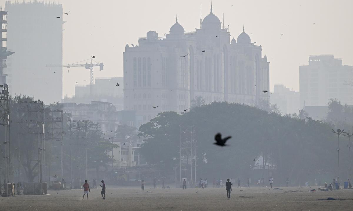 People walk at Girgaon Chowpatty as city skyline is seen engulfed in smog on December 5, 2025.