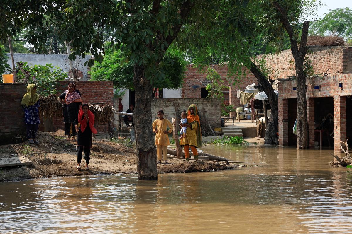 Residents stand at the premises of their house flooded due to the monsoon rains and rising water level of the Sutlej River in Hakuwala village near the Pakistan-India border in Kasur district of the Punjab province, Pakistan, on August 23, 2025.