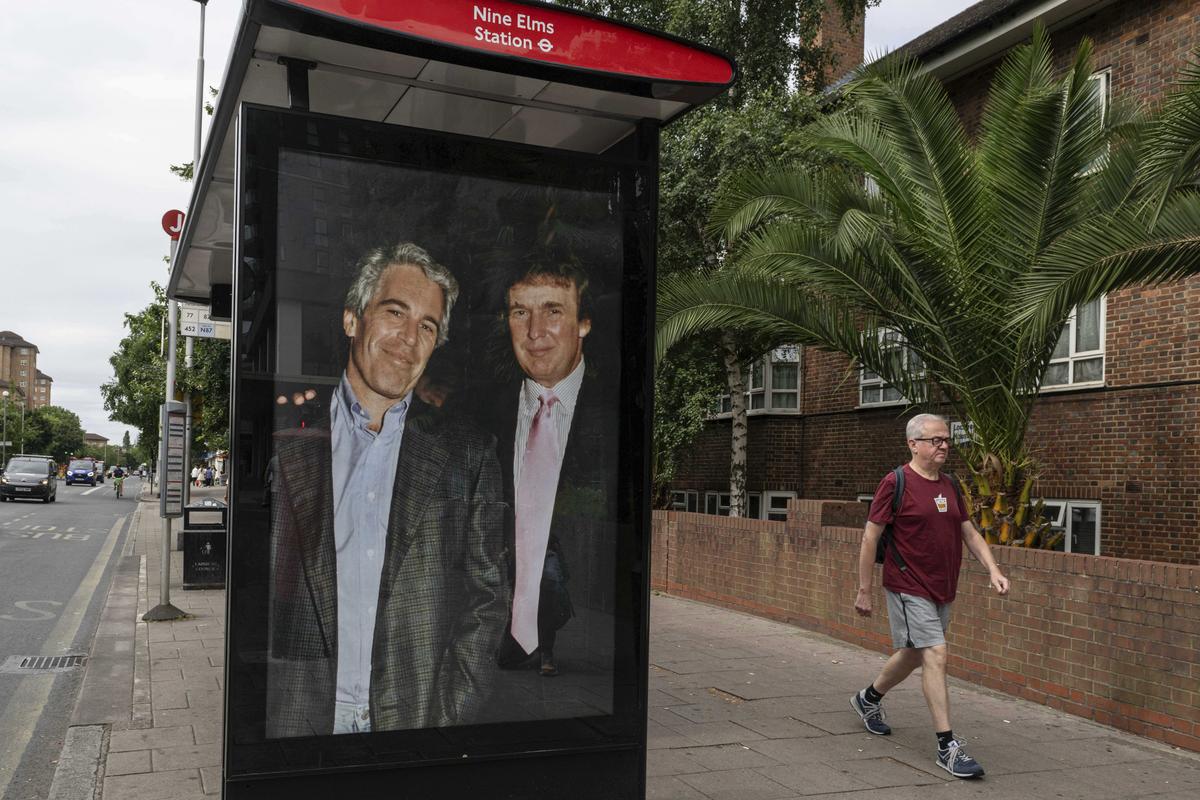 Os passageiros passam por um ponto de ônibus perto da estação Nine Elms enquanto ativistas colocam um cartaz mostrando o presidente Donald Trump e Jeffrey Epstein perto da Embaixada dos EUA em Londres, quinta-feira, 17 de julho de 2025.
