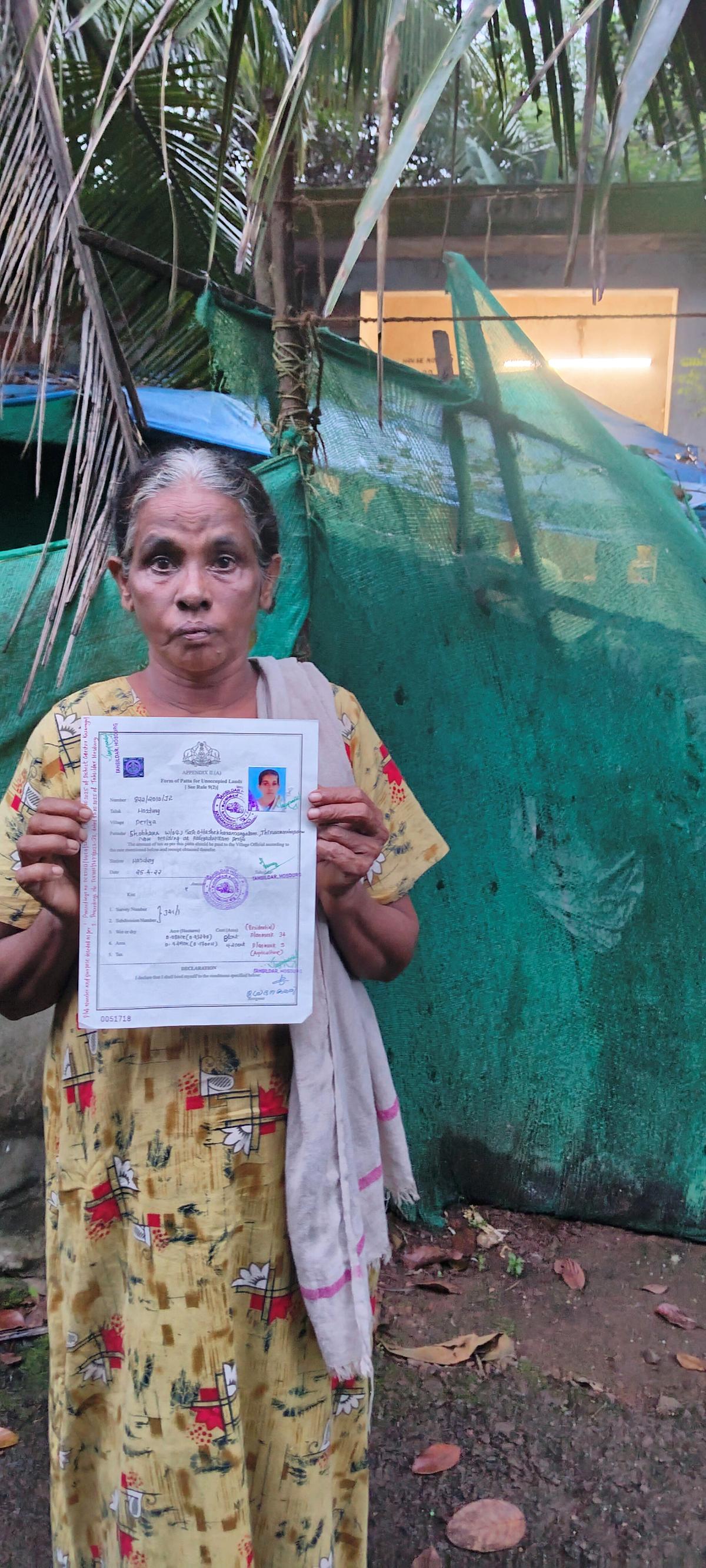 Shobana Kumari of Nalakara, Pullur-Periye panchayat, holding her title deed issued in 2022 and reissued a month back in front of her house in the Chengara resettlement colony.  