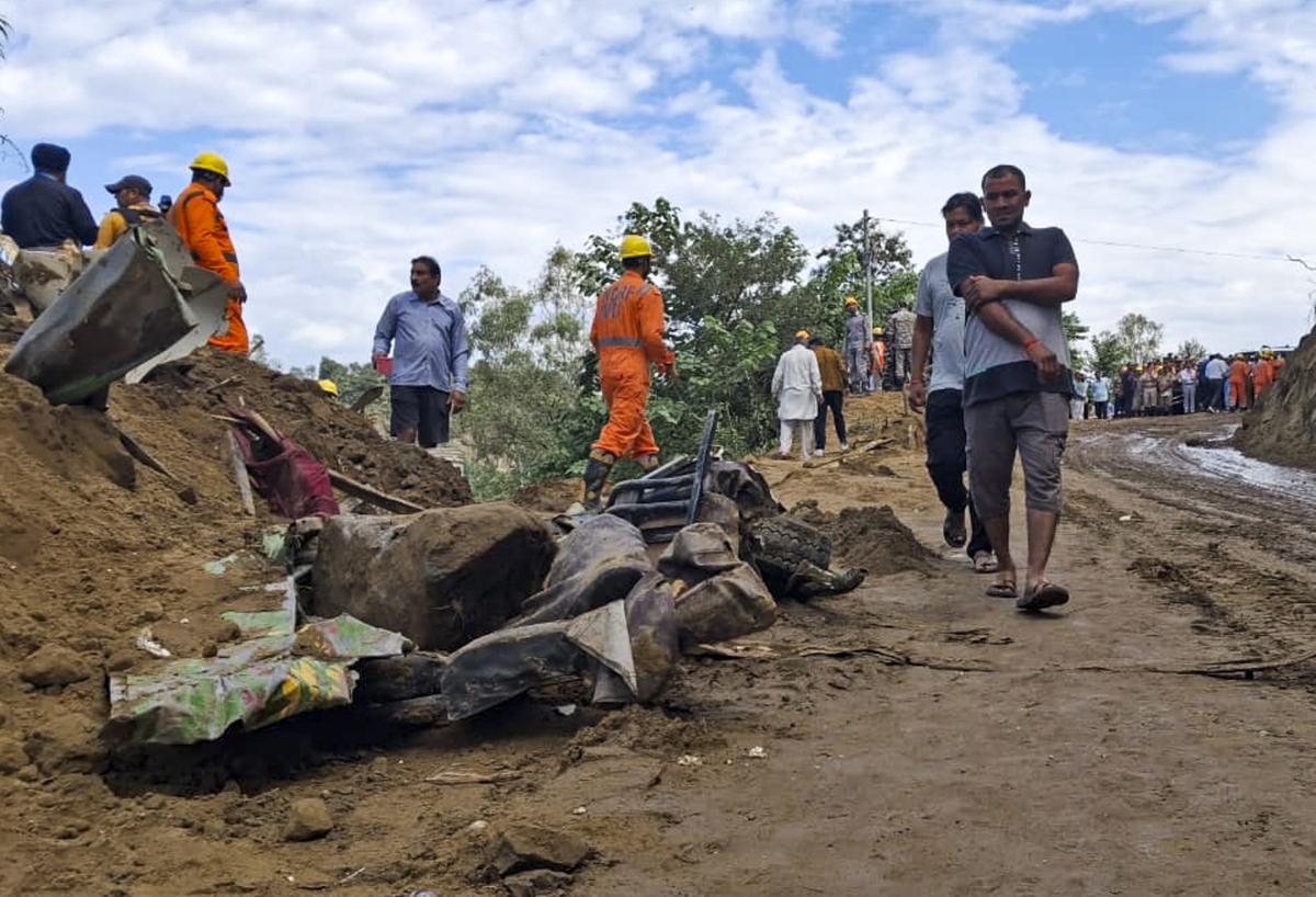 People walk past the damaged remains of a bus lying in debris in Bilaspur