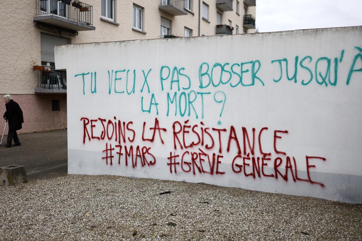 An elderly woman walks past graffitis reading “You want to work until death? Join resistance, General Strike on March 7” in Strasbourg eastern France, Sunday, March 5, 2023. 
