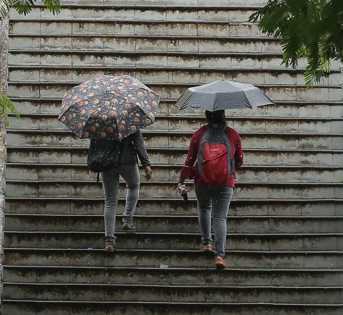 Commuters climb the steps of the Rainbow Bridge at Marine Drive in Kochi, umbrellas in hand, amid rain on Wednesday.