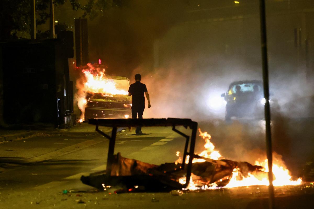 A person stands near a burning vehicle as unrest continues following the death of a 17-year-old teenager killed by a French police officer during a traffic stop, in Nanterre, Paris suburb, France on July 1, 2023.