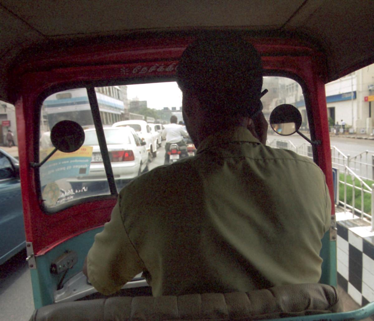 চলার সময় মোবাইল ফোন ব্যবহার করে একটি অটোরিকশা ড্রাইভার।