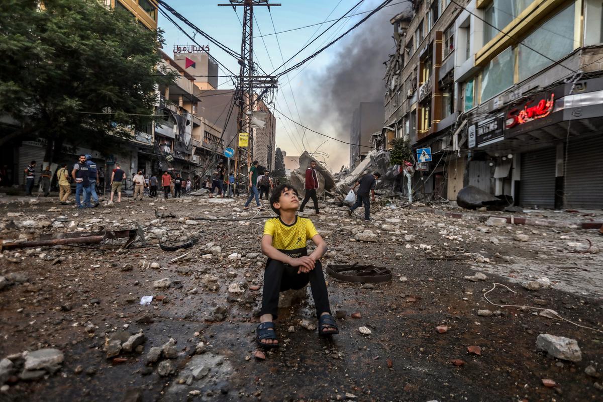 A boy sitting in the middle of the street witnessing the destruction that occurred in one of the main commercial streets in Gaza 