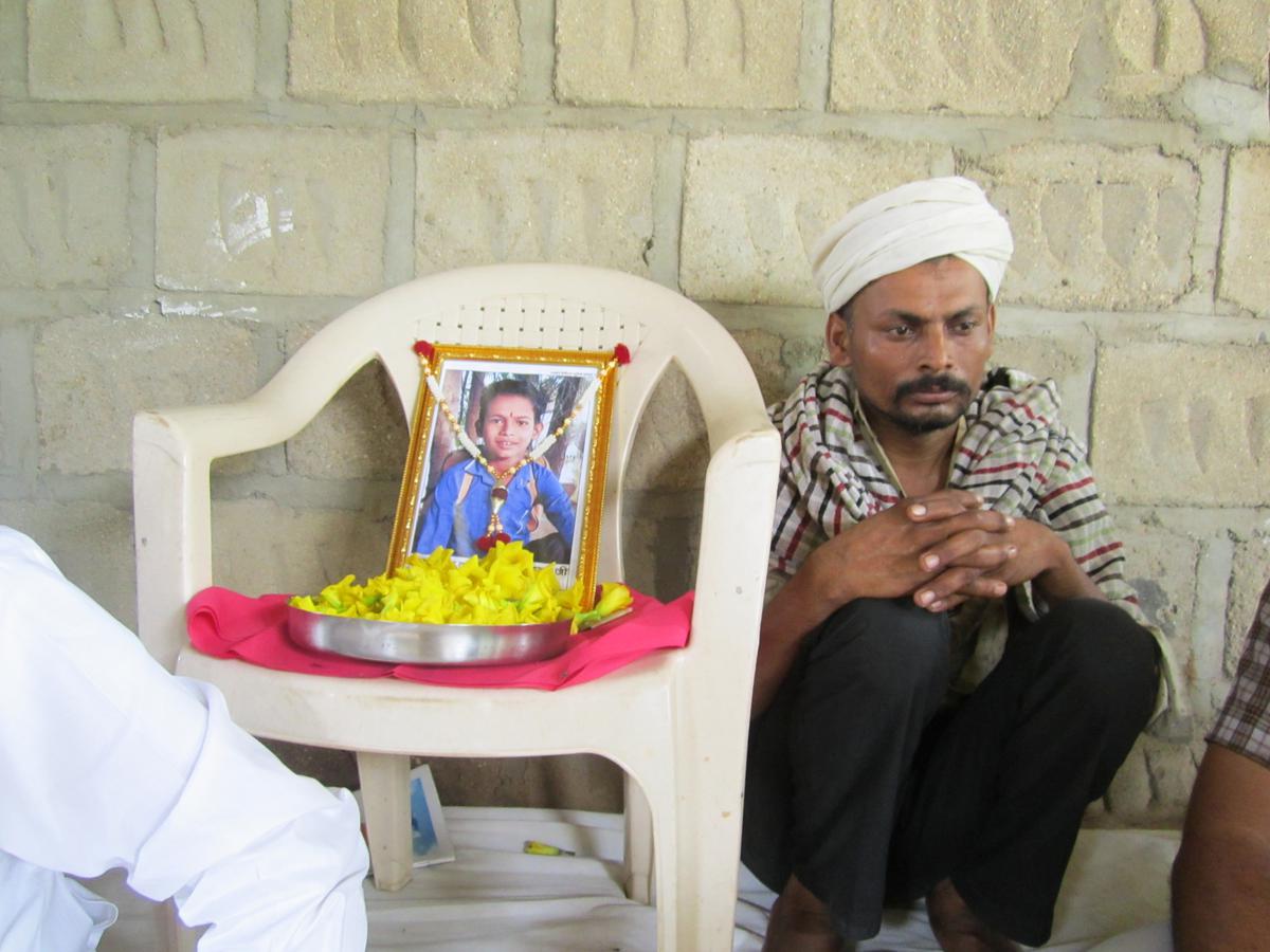 Devaram Meghwal grieving next to the photo of his deceased nine-year-old son, Inder, at the house of his brother on the outskirts on Surana village.