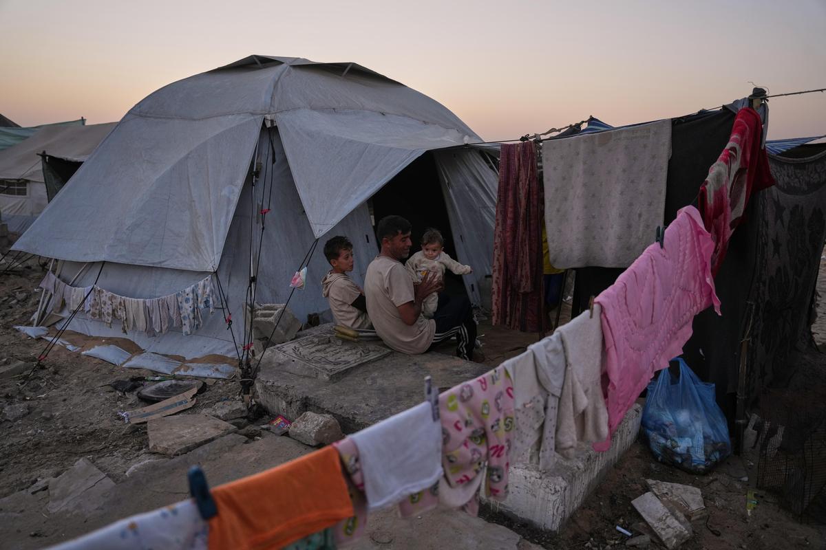 Mohammed Barabakh sits on a grave with his children at the entrance to his tent, that was set up in a cemetery in Khan Younis, in the southern Gaza Strip, on Friday, Oct. 31, 2025.