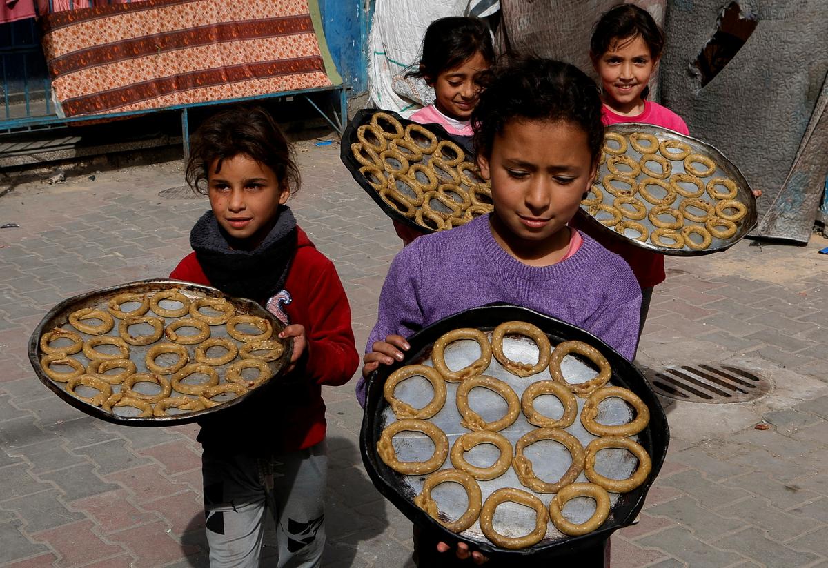 The displaced Palestinian children hold trays while preparing traditional sweets for Eid al-Fitr holidays, which marks the end of the month of Muslim Holy Fast of Ramadan, in Khan Youis in the strip of southern Gaza on March 29, 2025. 