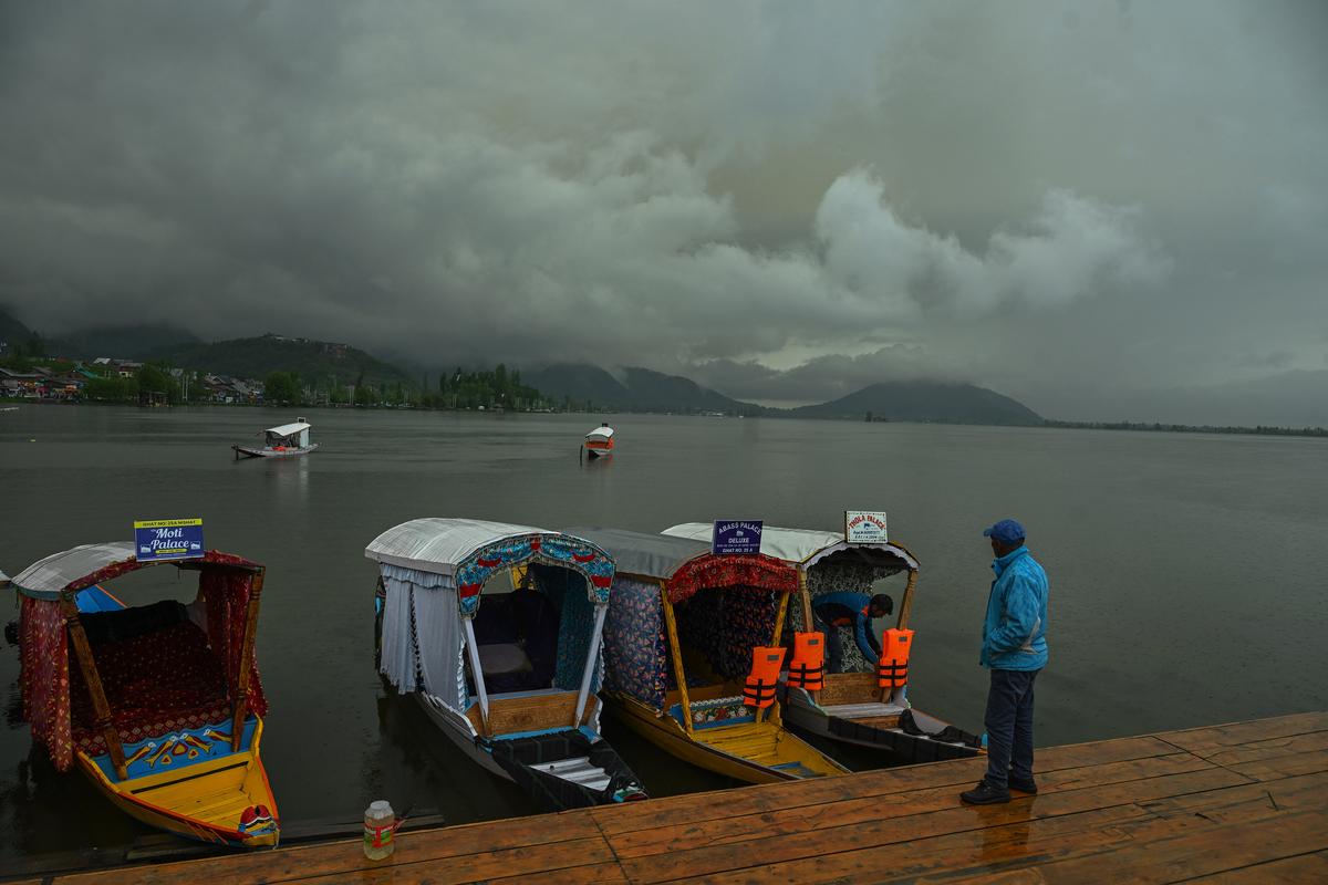 A boatman stood next to Shikaras during rainfall in Srinagar on April 19, 2025.