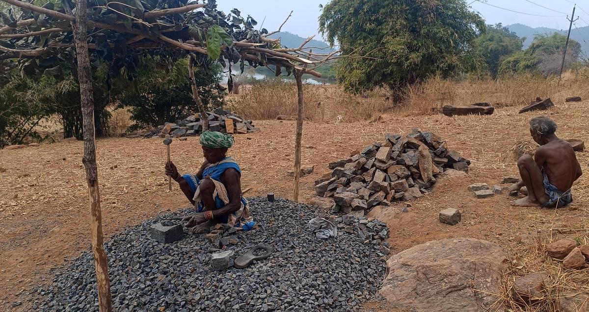 Il materiale da costruzione deve essere trasportato attraverso il bacino idrico e poi trasportato in salita dai residenti nel panchayat di N. Podapadar, nel distretto di Kalahandi. Qui stanno abbattendo le pietre per facilitarne il trasporto.