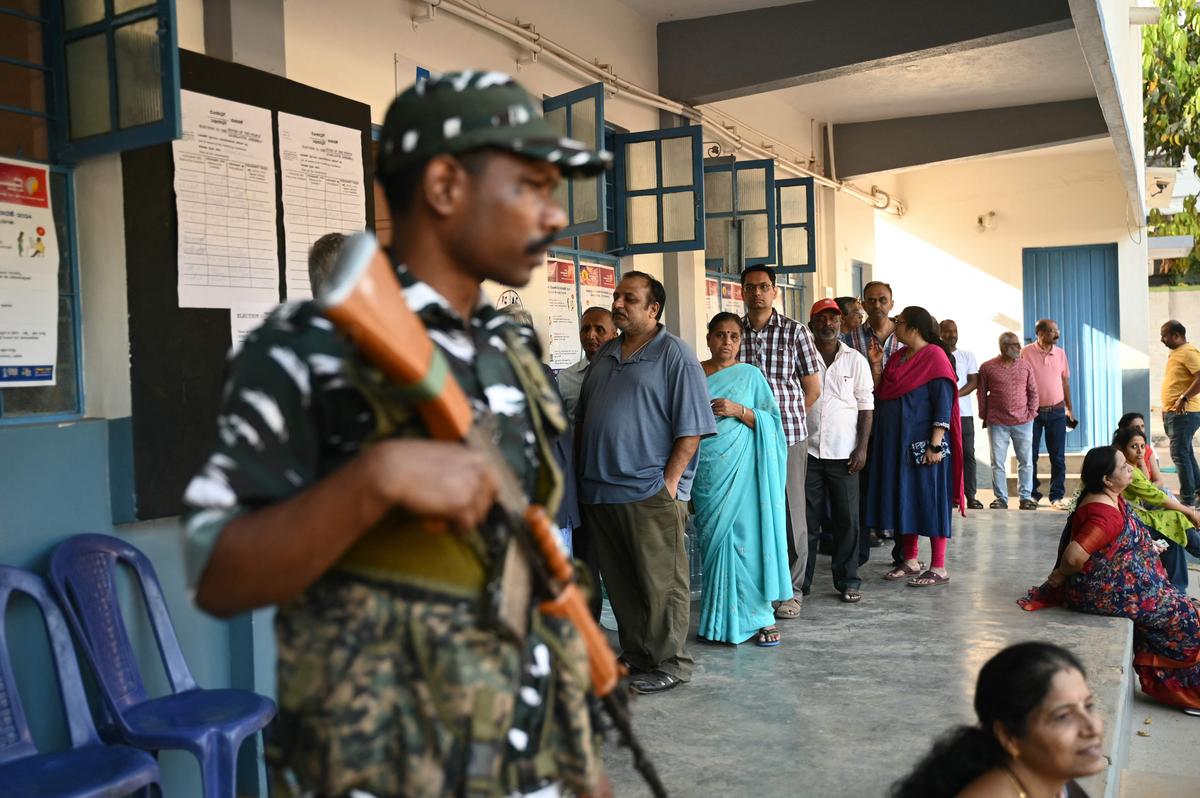A security personnel stands guard as voters queue to cast their ballot outside a polling station during the second phase of voting of India’s general election in Bengaluru on April 26.