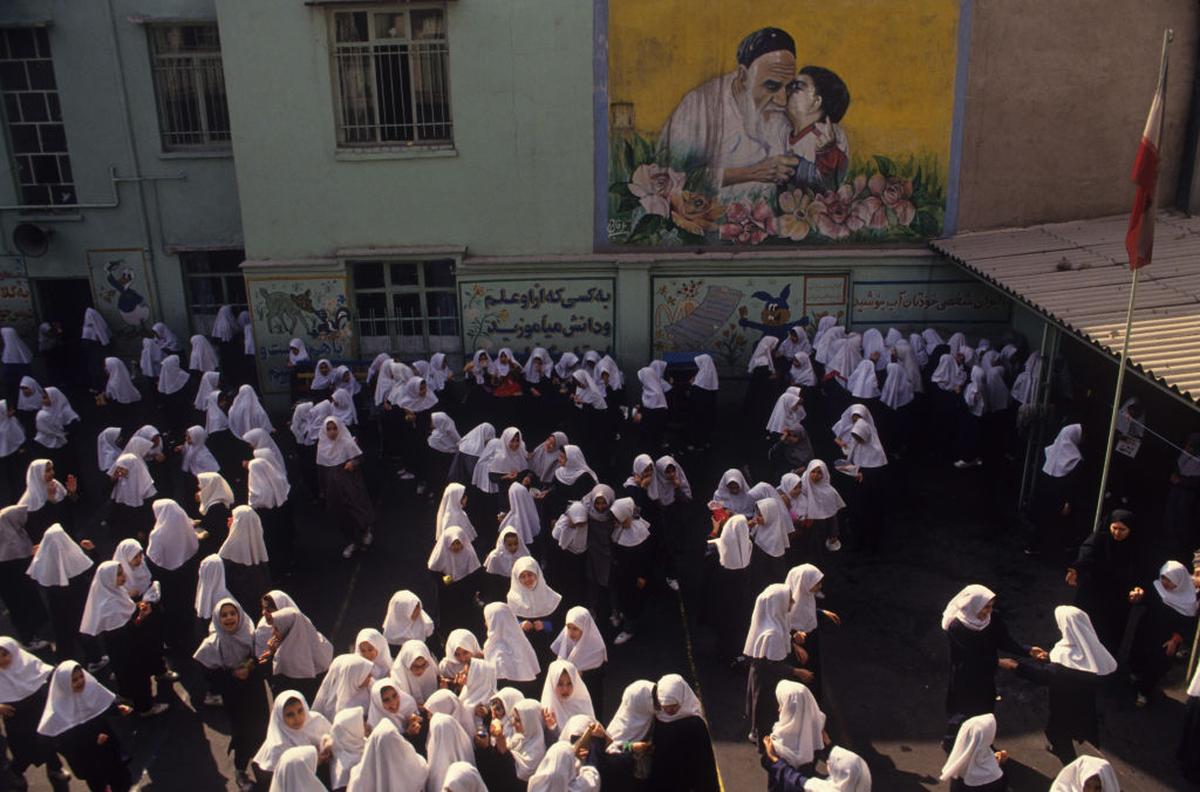 Meninas no pátio da escola sob um mural do Aiatolá Khomeini em Teerã, 1997. Meninas no pátio da escola sob um mural do Aiatolá Khomeini em Teerã, 1997.