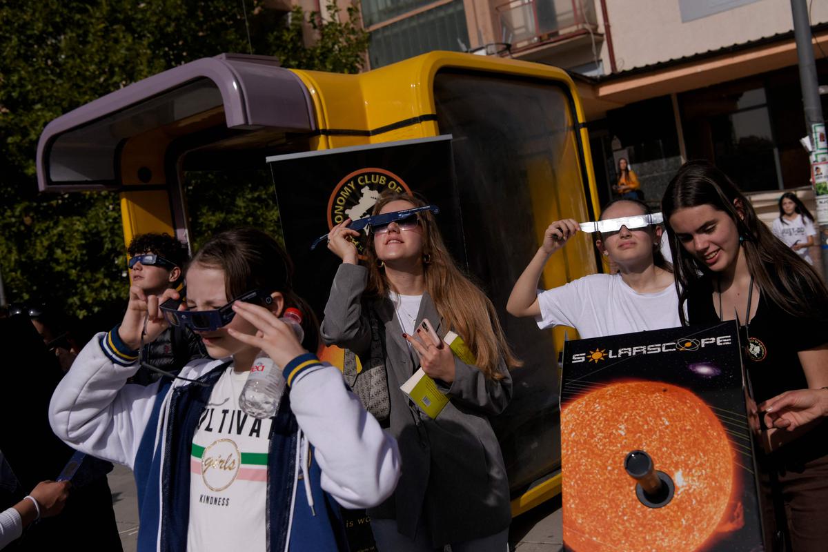 People use protective glasses to watch a partial solar eclipse in Pristina on October 25, 2022. 