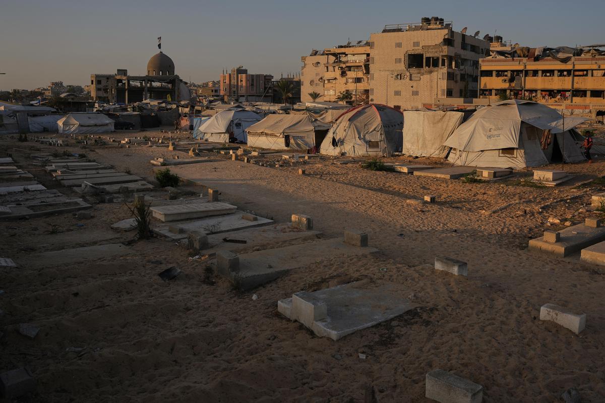 Makeshift tents for displaced Palestinians are seen set up next to graves in a cemetery at sunset in Khan Younis, in the southern Gaza Strip, on Friday, Oct. 31, 2025. 