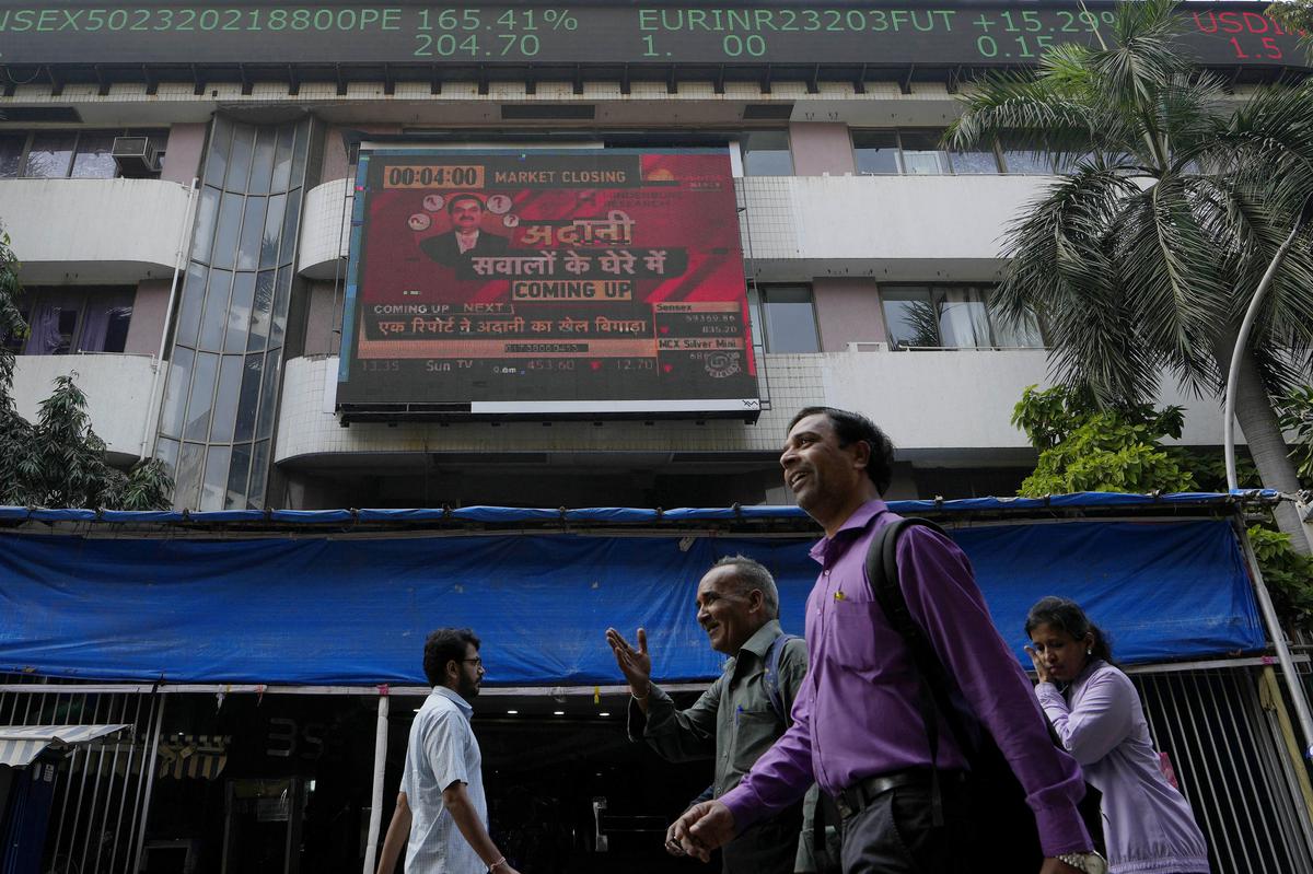 People walk past an electronic display featuring news about Adani Group outside the Bombay Stock Exchange building in Mumbai on January 27, 2023. 