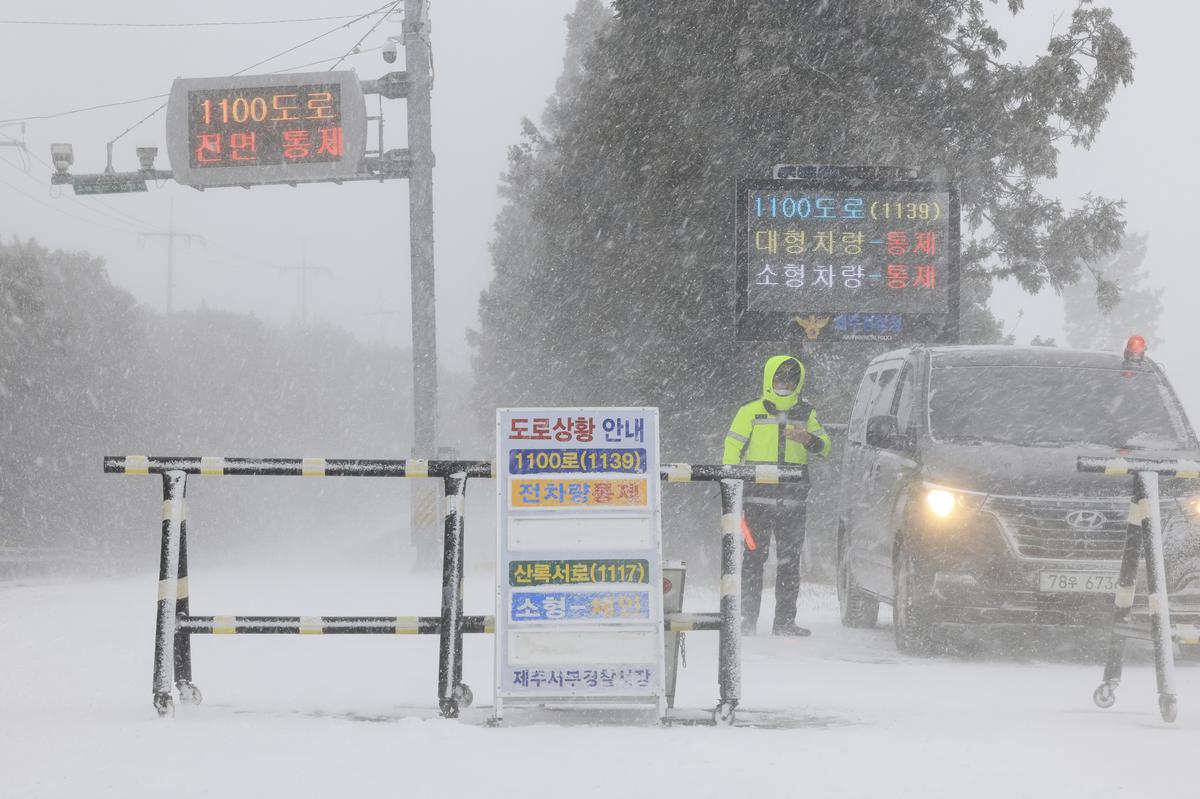 A police officer controls the entry of vehicles at a road amid heavy snowfall on Jeju Island, South Korea 