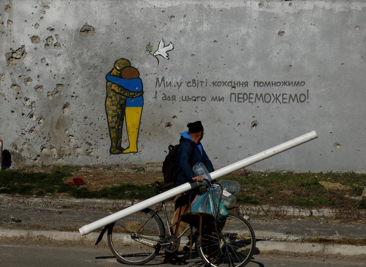 A man rides a bicycle past a painting on the wall of a building riddled with bullets and rubble, during the Russian invasion of Ukraine, in the recently recaptured town of Kupiansk, Ukraine.