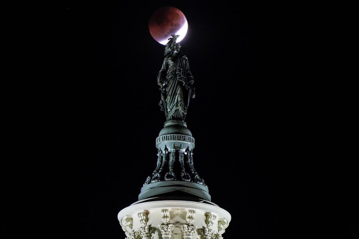 A lunar eclipse is seen behind the Statue of Freedom on the U.S. Capitol Dome in Washington, U.S., November 8, 2022. Known as a blood moon, it appears a reddish-orange from the light of Earth’s sunsets and sunrises. 