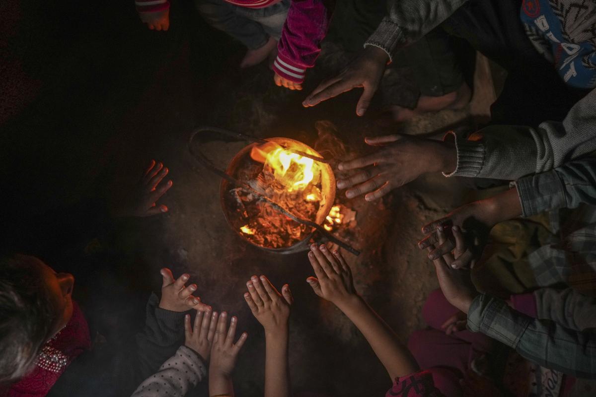 Reda Abu Zarada, 50, displaced from Jabaliya in northern Gaza, warms up by a fire with her grandchildren at a camp in Khan Younis, Gaza Strip, on December 19, 2024.