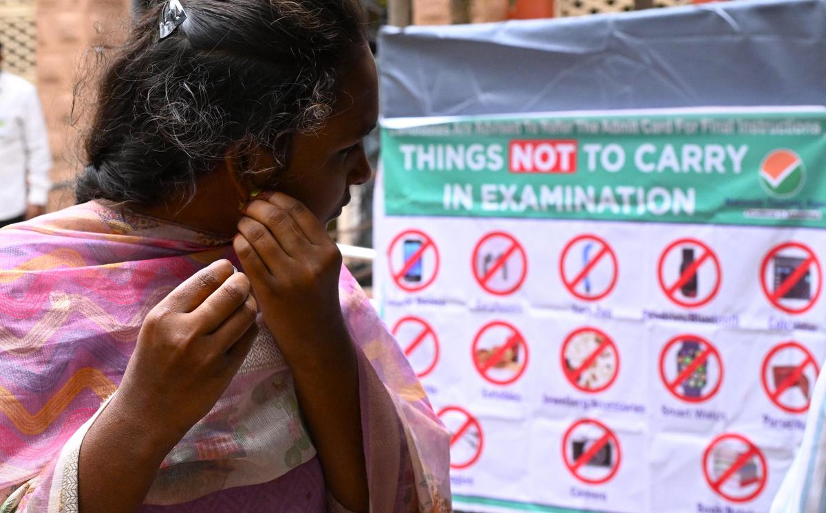 Uma candidata que concorre ao NEET tira os brincos antes de entrar no centro de exames da AU College of Engineering, em Visakhapatnam, no domingo.