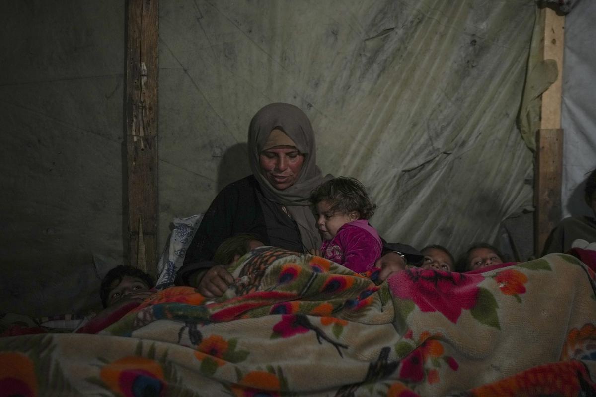 Reda Abu Zarada wraps herself and her grandchildren in blankets as they prepare to sleep in their tent at a camp in Khan Younis, Gaza Strip, on December 19, 2024.