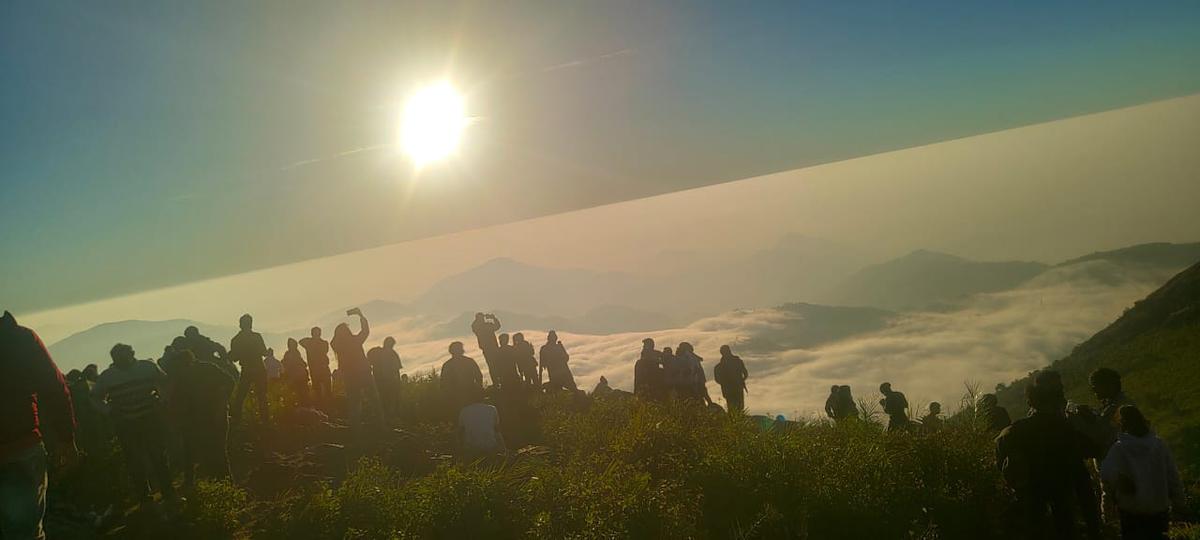 Visitors enjoying the view of the sun rising above a thick blanket of clouds from the hill top at Vanjangi Hills.