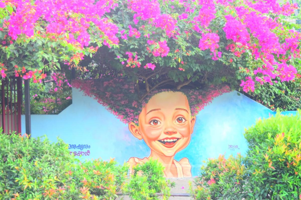 A wall art on the roadside wall of a house in Thiruvananthapuram featuring pink bougainvillea and a headshot portrait