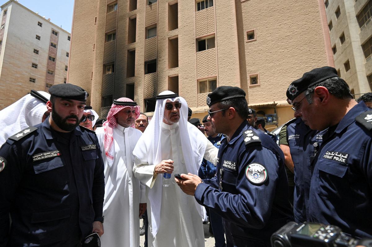 Kuwait’s Deputy Prime Minister and Minister of Defence and acting Interior Minister, Fahad Yusuf Al-Sabah speaks with police officers in front of a burnt building, following a deadly fire, in Mangaf, southern Kuwait on June 12, 2024. 